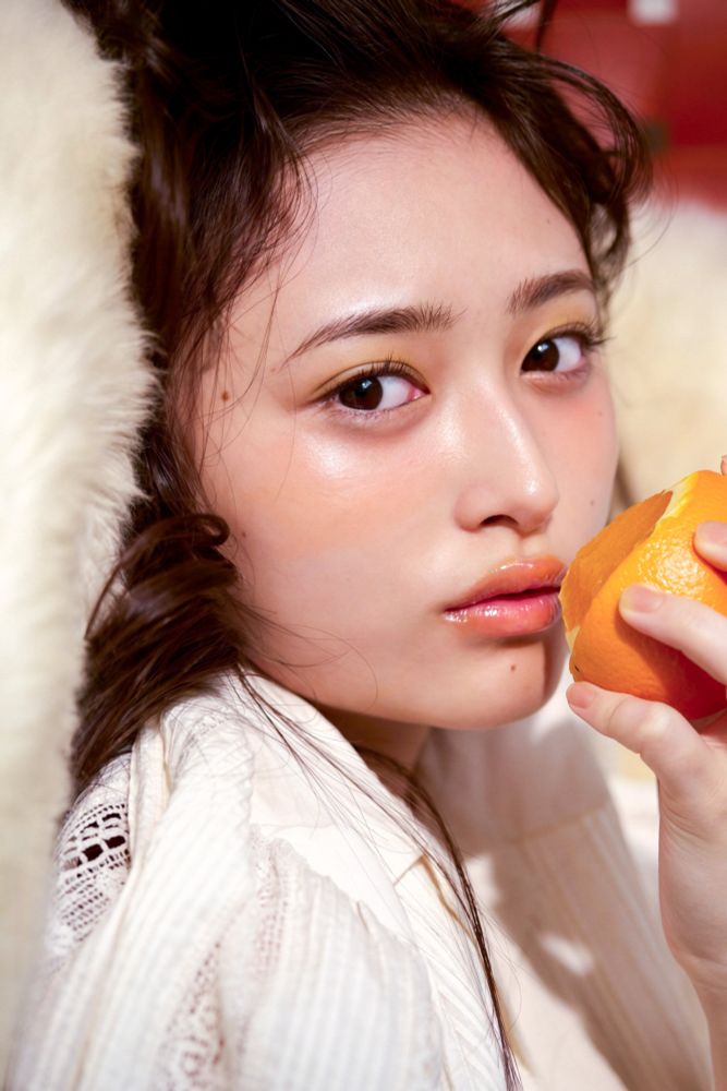 Nagi lying down in that same rug/blanket and with that same makeup, this time bringing the orange near her lips