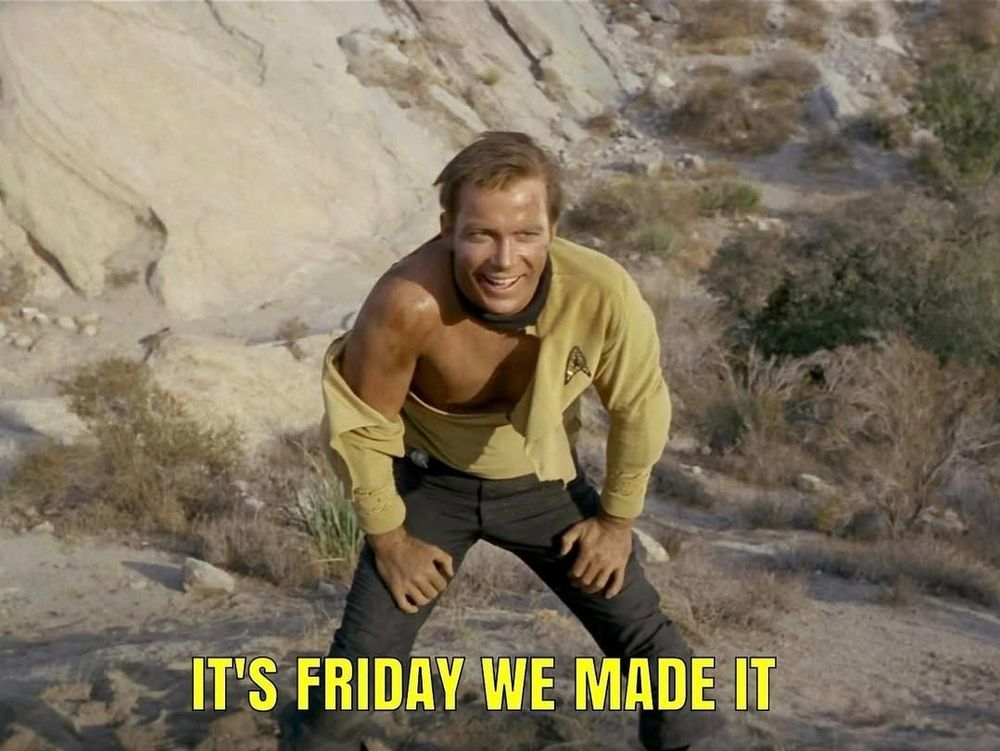 Captain Kirk, from Star Trek TOS, is standing in front of a rocky landscape. He is hunched over with his hands on his thighs, like he's catching his breath. His Starfleet uniform is so torn up and destroyed that half of his chest is visible amongst the ripped flaps of fabric. His hair is messed up and he's covered in a layer of dirt and grime. But despite all of that, he's got a wide and wild grin on his face, giving him an expression like he's thinking "bring it on." A large caption in yellow font at the bottom of the image reads: IT'S FRIDAY WE MADE IT