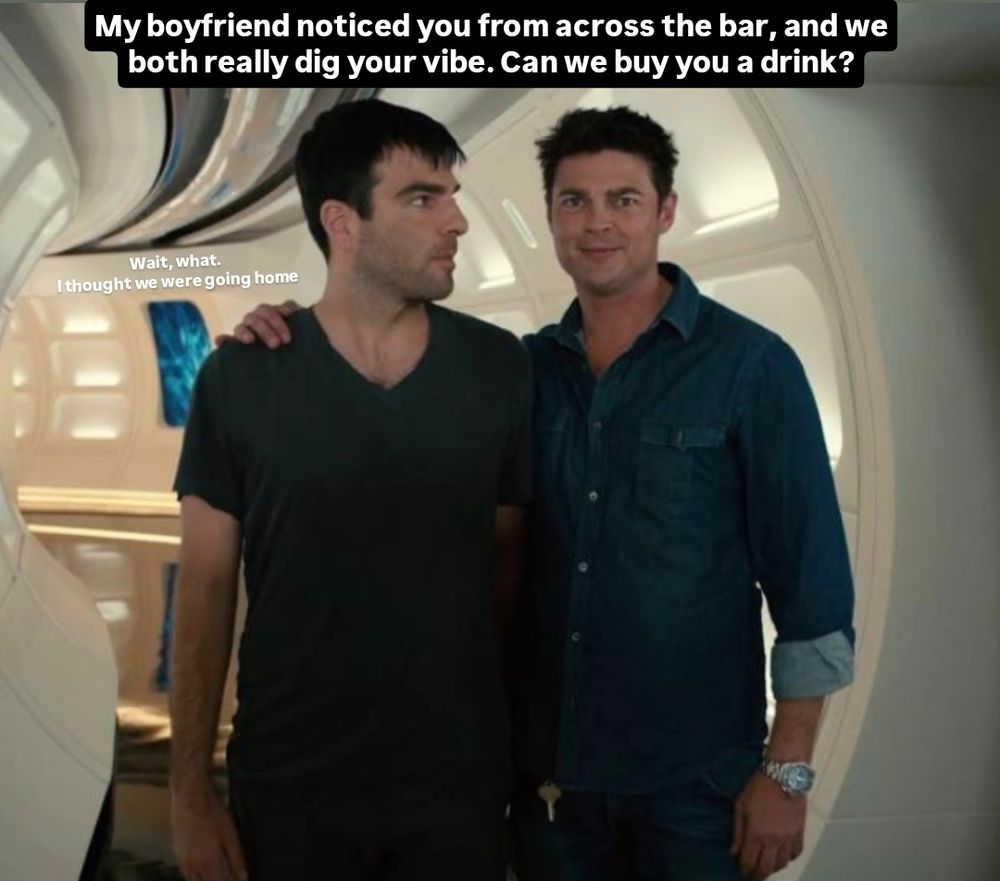 A behind the scenes photo from Star Trek (2009) of Zachary Quinto and Karl Urban, who play Spock and Bones, in a corridor on The Enterprise. They are standing side by side, and Karl is gripping Zach's far shoulder in a one armed hug as he looks directly into the camera with a dainty, close-lipped little smile. Zachary has his arms down and is looking at Karl like he just said something unexpected. Text has been crudely edited onto the top of the image: "my boyfriend noticed you from across the bar, and we both really dig your vibe. Can we buy you a drink?" next to Zach is much smaller text, as though he is replying: "wait, what. I thought we were going home"