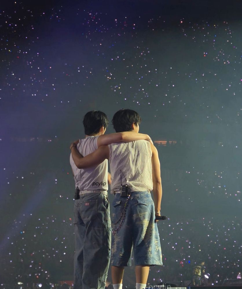 from behind, leeknow and han with arms around each other, against the sea of glittering lights across the stadium