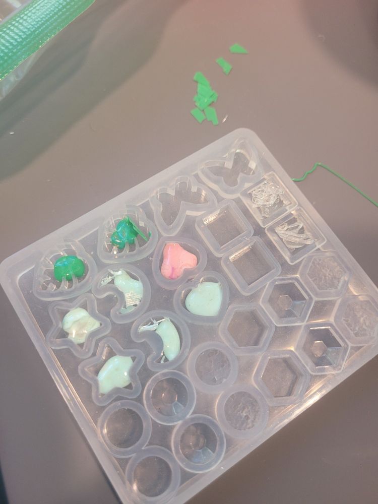 Partially melted PLA in the small charms silicone mold. Small flakes of green PLA await placement inside.