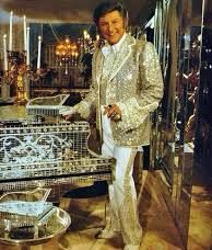 Singer Liberace draped in gold in a gold room with a gold piano. 