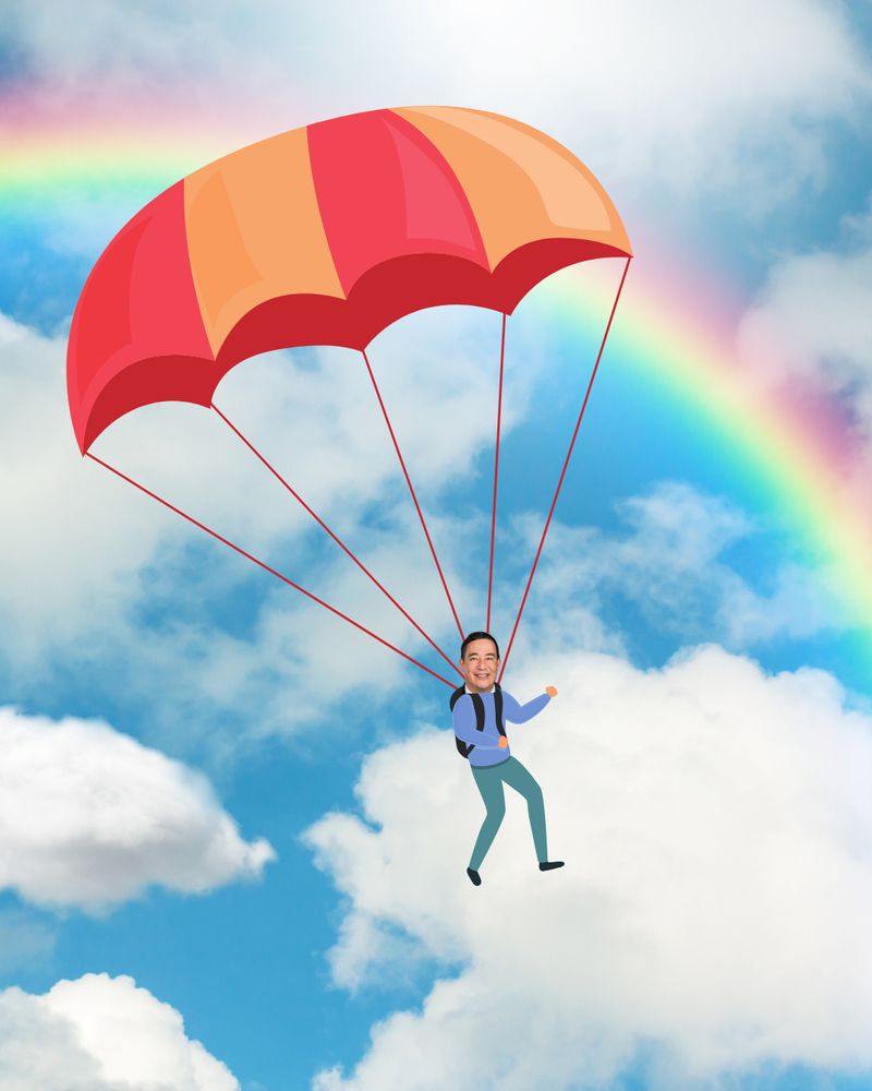Sec. Hobbs parachuting with a vibrant orange and red parachute against a blue sky with fluffy clouds and a colorful rainbow in the background.
