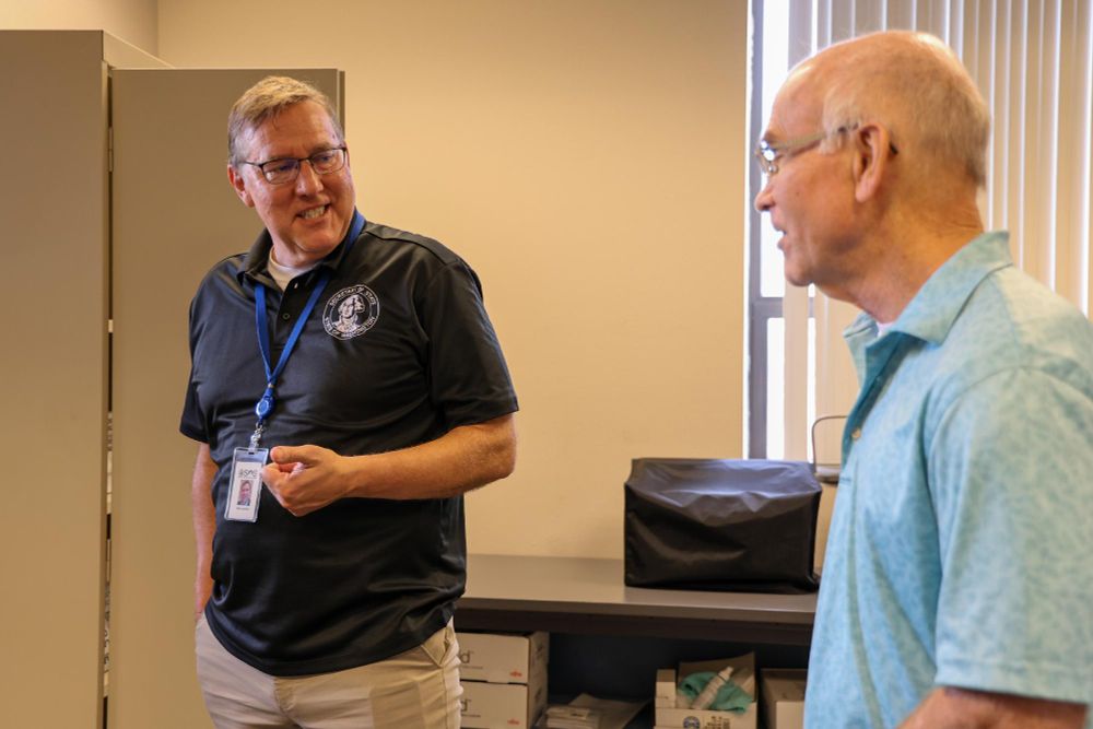 Two individuals in conversation, one wearing a shirt with a OSOS logo and a badge, in an office setting.
