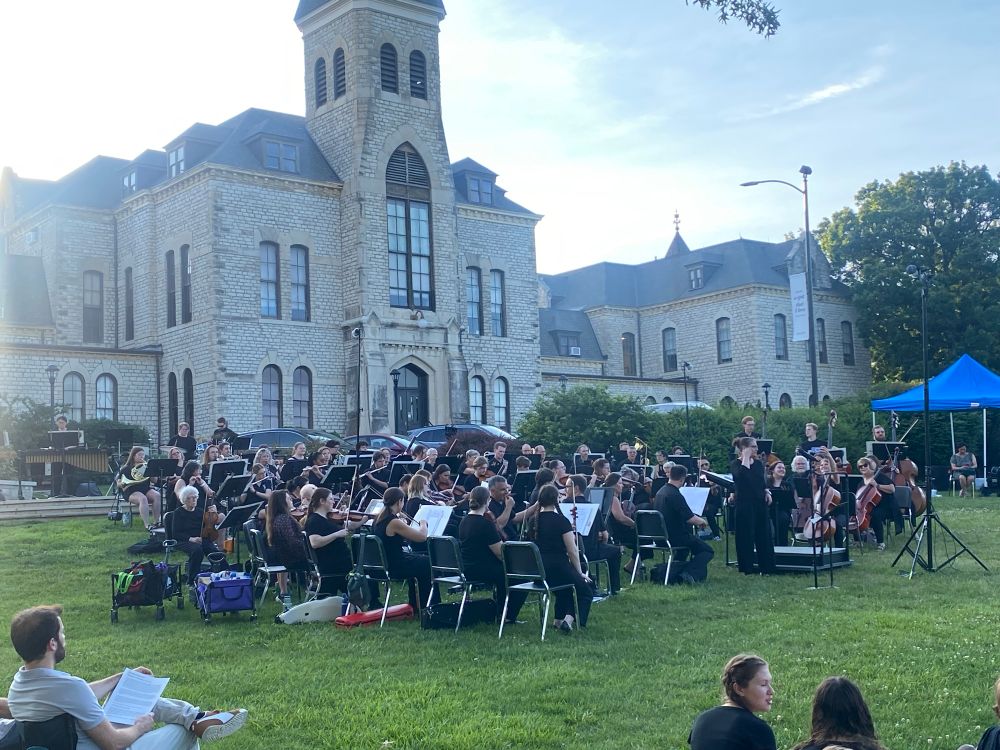 Symphony musicians playing on lawn,  in front of campus admin hall. 