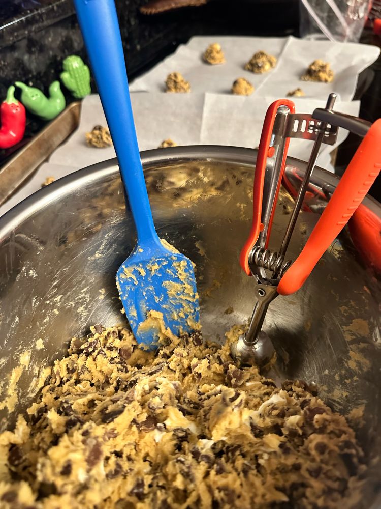 Cookie dough in a bowl with a spatula and small scooper 