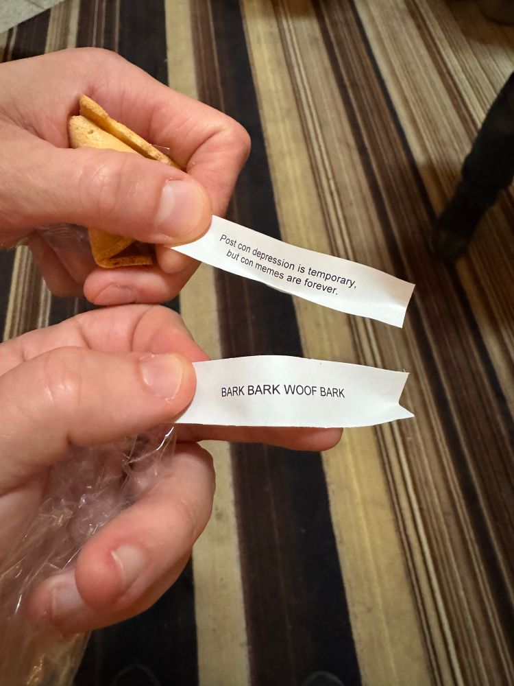 Picture of two hands holding messages from a fortune cookie that each read “Post com depression is temporary, but con memes are forever” and “BARK BARK WOOF BARK”