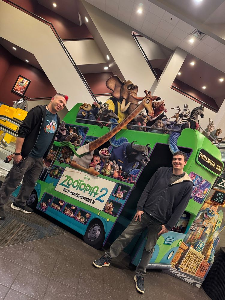 Picture of two people standing in front of a giant zootopia 2 movie display in a theater.