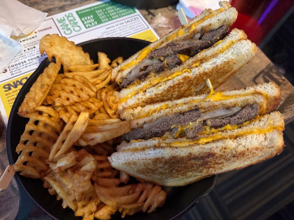 Picture of a patty melt but with grilled cheese sandwiches as the buns and a side of waffle fries.
