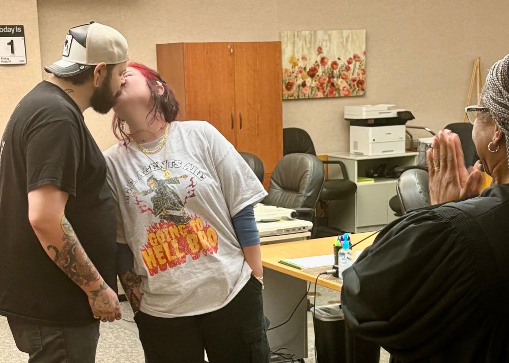 Couple kissing at courthouse wedding. Bride wearing a t-shirt that reads “I.C.E. Agents Are Going to Hell Bro.”