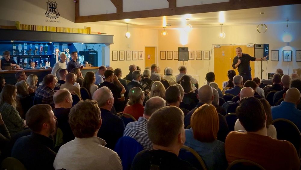 A handsome comedian entertains a crowd of his peers.