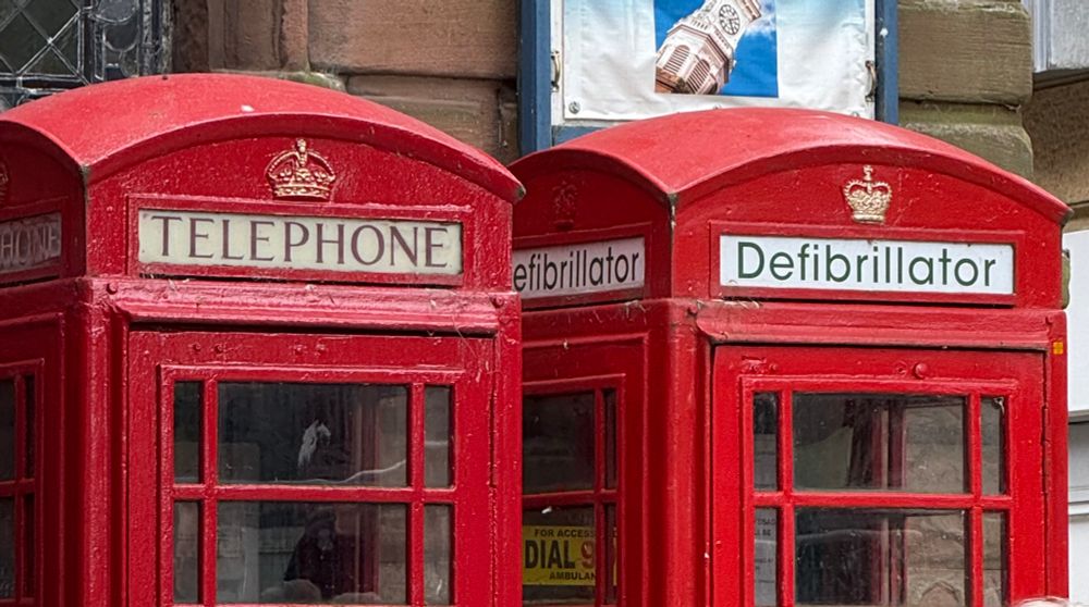 Two red phone boxes alongside each other.
One has a sign reading “Telephone”, the other says “Defibrillator”.
