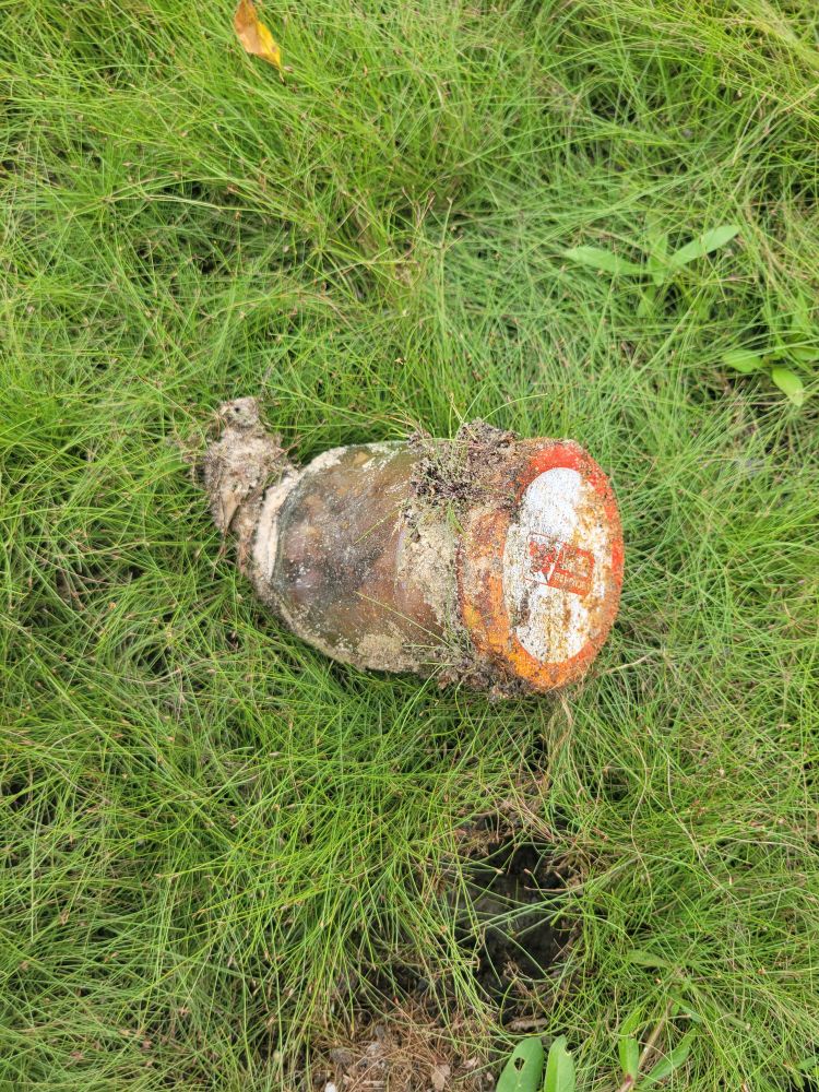 A clear jar covered in dirt, with cloudy reddish-brown innards. It has a rusty white and red trimmed metal lid.