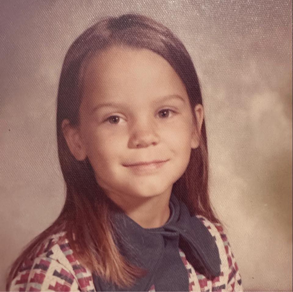 A photo of me as a young child. Long, brown hair, 70's style, thick collared shirt. Smiling. 