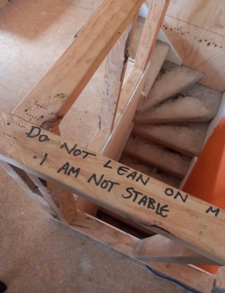 A rickety railing above a steep staircase. someone has written on it, do not lean on me. I am not stable