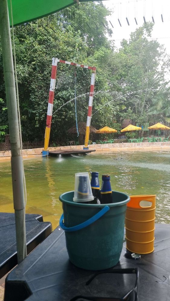 uma piscina de água doce ao fundo, uma mesa com garrafas de cerveja em um balde em primeiro plano