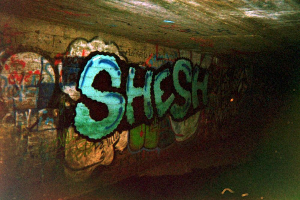 "shesh" in big letters with a wiggly outline, inside a concrete sluice gate