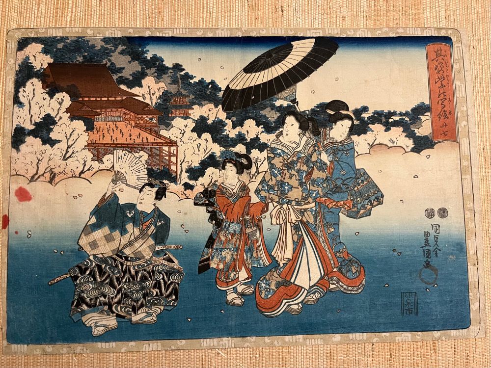 An ukiyo-e print with a deep blue to white gradient starting at the bottom and a temple in the background among sakura trees. In the foreground are several ornately dress figures, a man on the left holding up a hand fans and three women on the right, one holding a black and white umbrella.