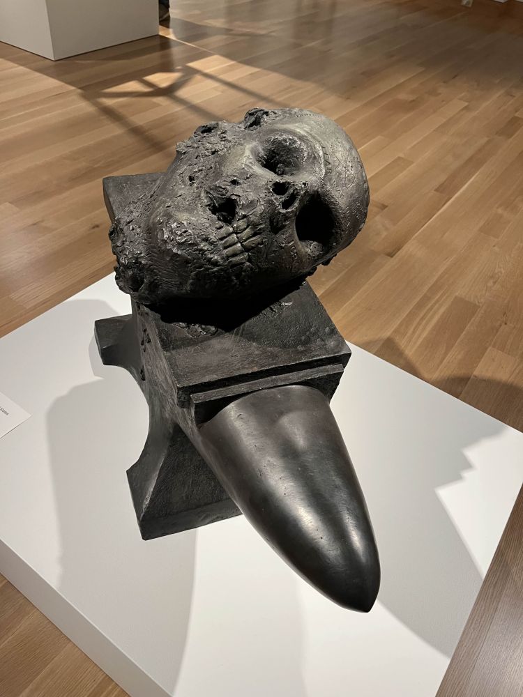 A bronze sculpture by Robert Arneson of a bullet-shaped anvil with a decomposing severed head on top of it.