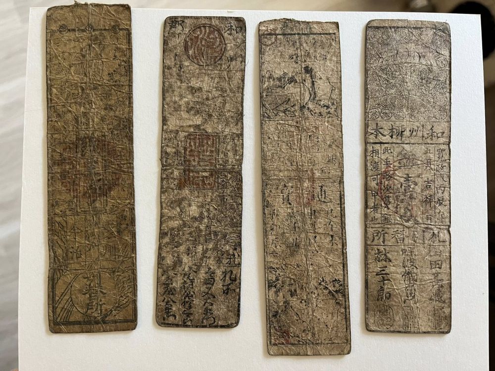 Four vertical strips of weathered paper with illustrations and writing in Japanese on them.