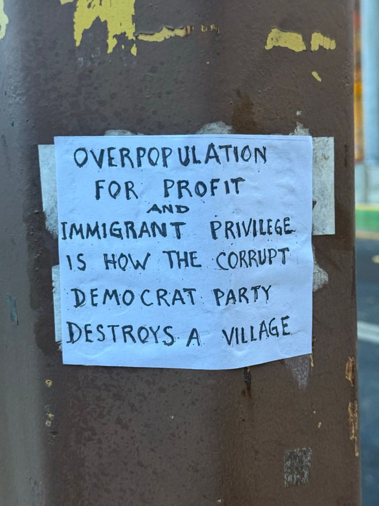 Handwritten sign on downtown Portland light pole reading 

Overpopulation for profit and immigrant privilege is how the corrupt democrat party destroys a village. 
