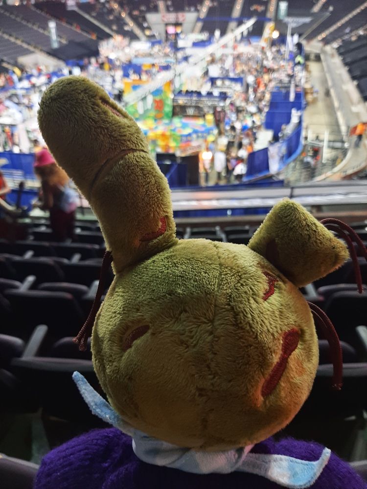 Photo of the back of Hex Springtrap doll's head. He is looking over rows of seating to a brightly lit vendor floor.