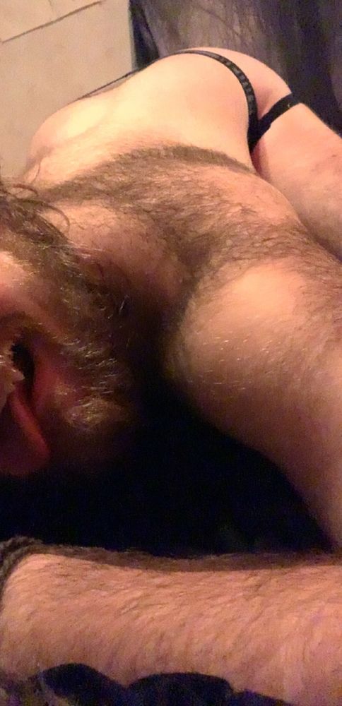 Picture of muscular hairy nonbinary person arching their back in a sexual manner lying on a bed