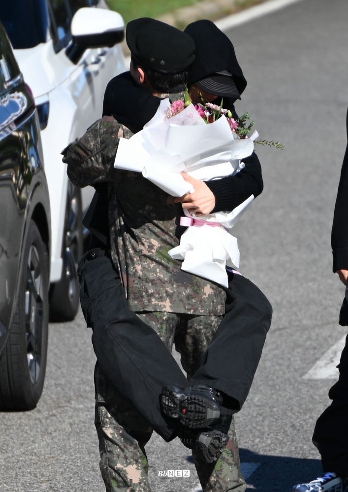 lee mihyuk do monsta x em sua cerimônia de dispensa do exército sul coreano abraçando outro membro do grupo, im changkyun, que traz consigo um buquê de flores