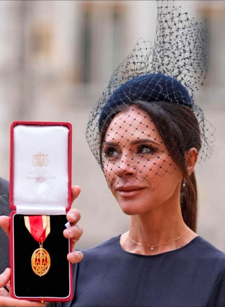 V Beckham giving her husband, who is displaying his medal to the press, at Buckingham Palace. 