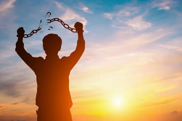 a man breaking the chains from his wrists in victory and in front of a sunset :)