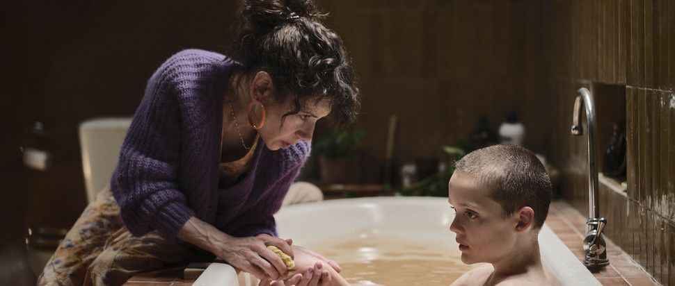 A screenshot from the movie "Bring Her Back" showing a brown-haired woman bathing a young boy
