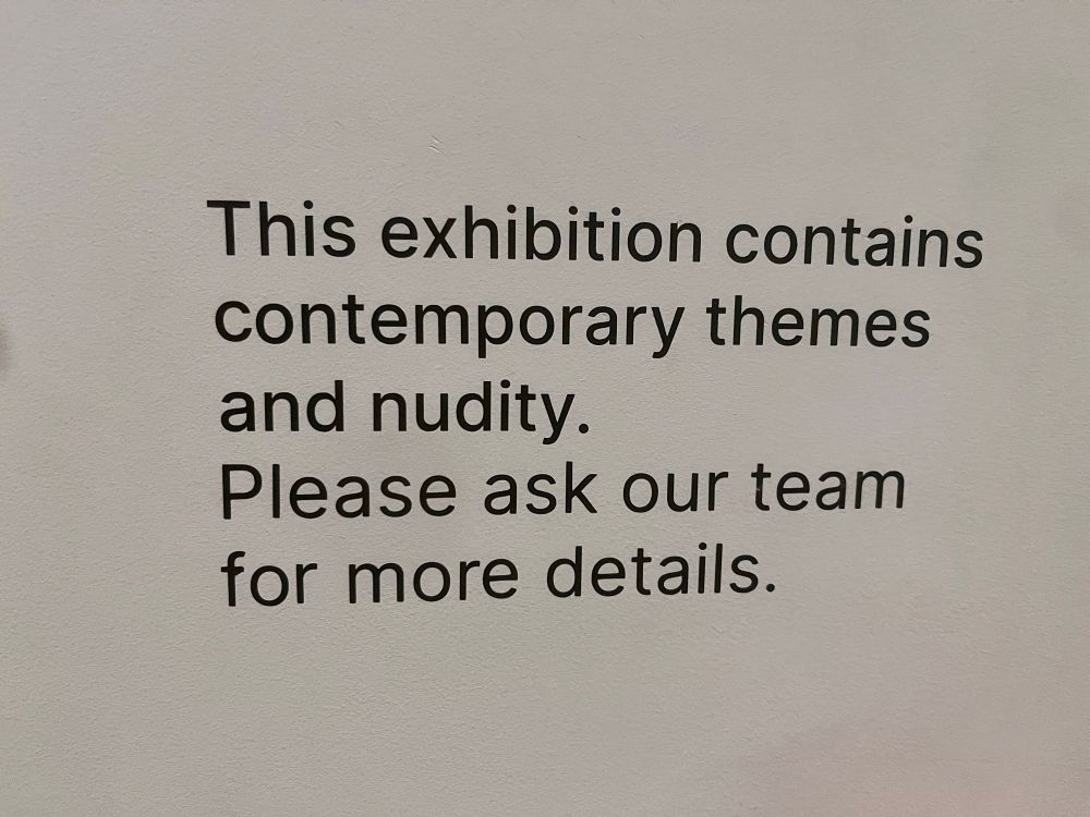 A wall text outside an exhibition: “This exhibition contains contemporary themes and nudity. Please ask our team for more details.”