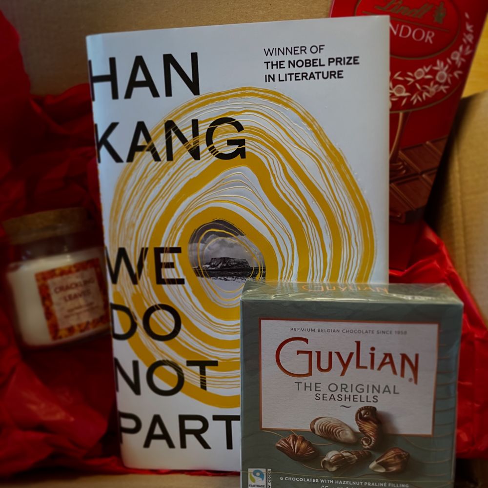 A gift box containing the hardback of We Do Not Part by Han Kang, with a scented candle, a Lindor chocolate bar and a box of Guylian chocolate seashells. 