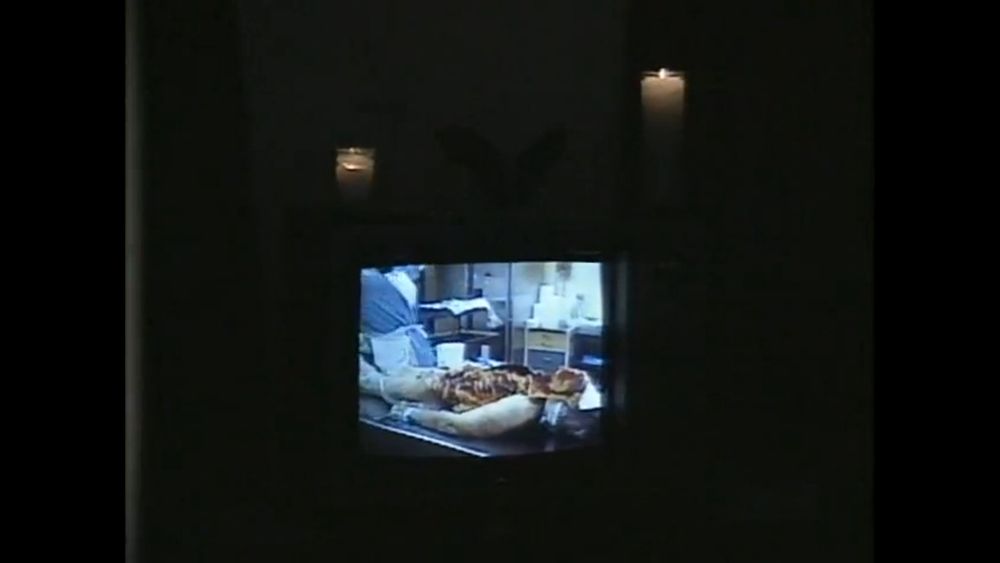 on a television flanked by candles, a video of a human being dissected plays