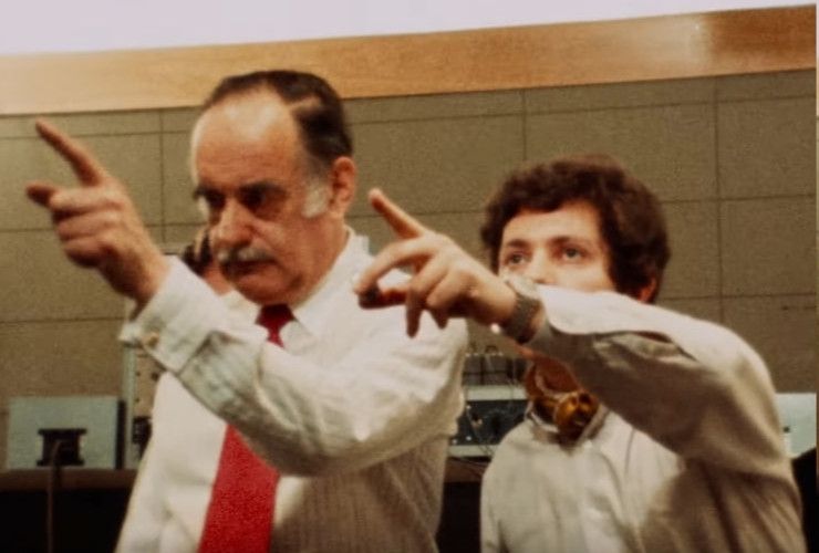 Two people from the Company cast recording documentary pointing towards the upper left corner.