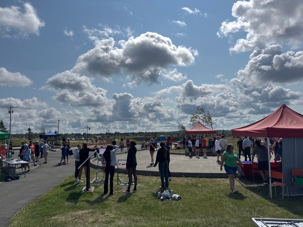 A sunny sky with lots of clouds and people milling about a paved area and with entertainment and tents