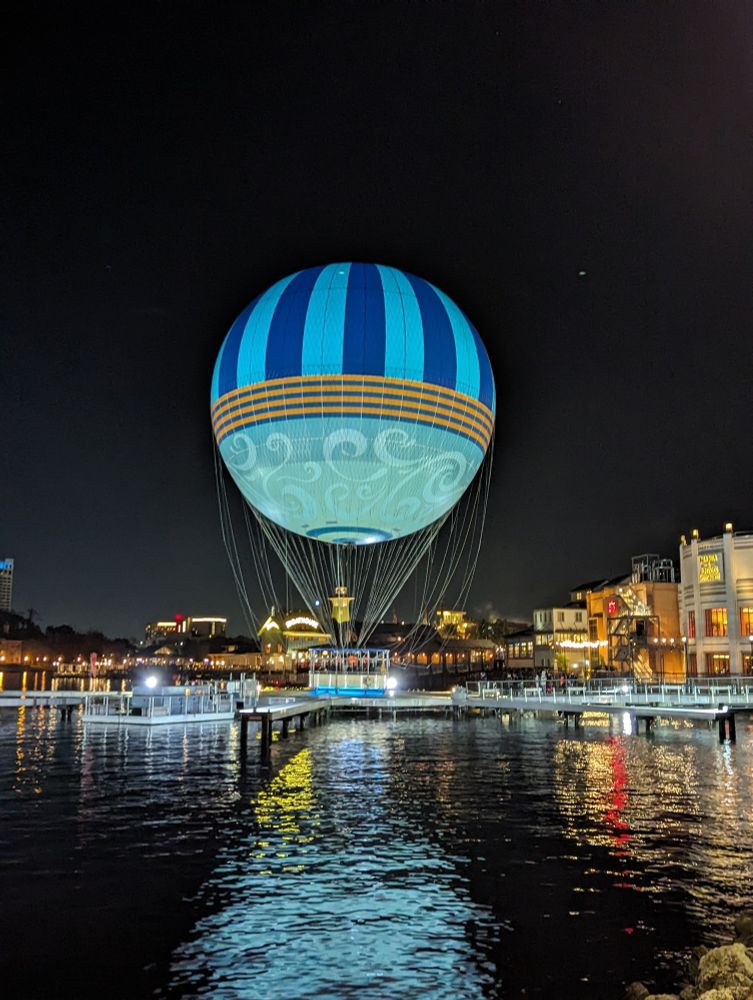 Disney hot air balloon, landed on the ground at night, reflecting the blue hues off the waters reflection.