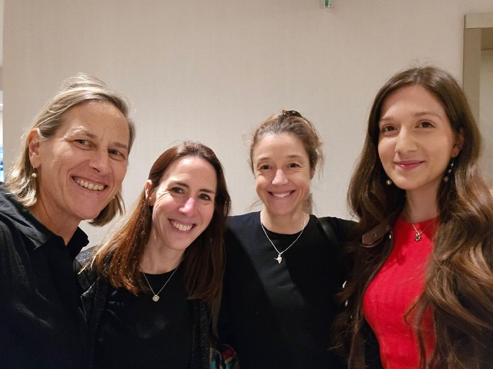 Four individuals smiling for a group photo in an indoor setting with a light background.
