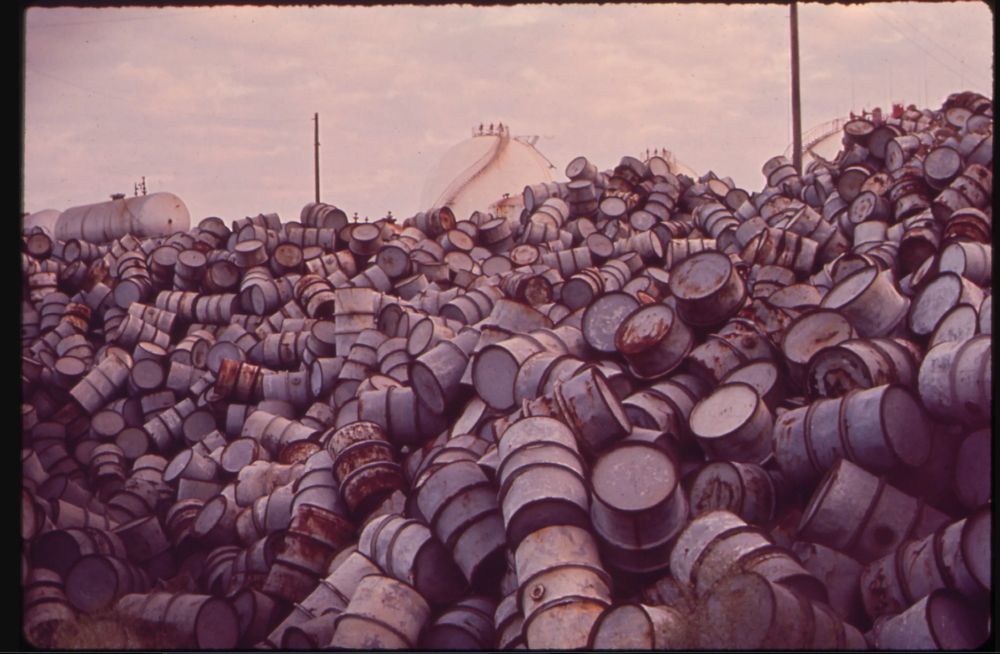 A vintage photo from the National Archives shows damaged oil drums piled high at an Exxon refinery. 