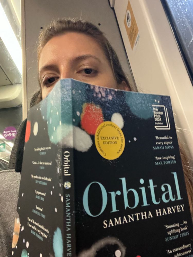 Girl on train holding up copy of Samantha Harvey's 'Orbital' 