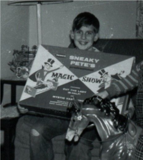 Seven y/o boy proudly holding Sneaky Pete's Magic Show in a b/w pic. On my left is my 1 y/o brother sitting on a plastic (?) rocking horse. Ripped and patched jeans were a bug, not a feature back then. 