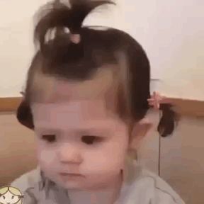 a baby girl with a ponytail on her head is making a sad face .