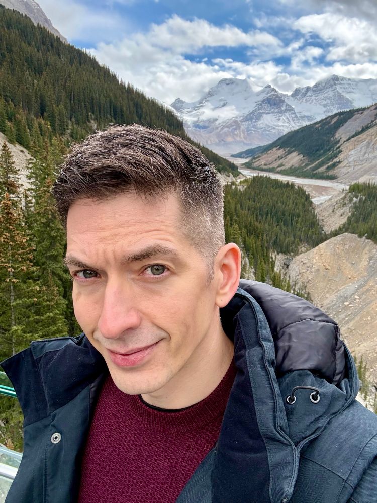 Aaron, peering into a camera against a rather breathtaking mountain view 