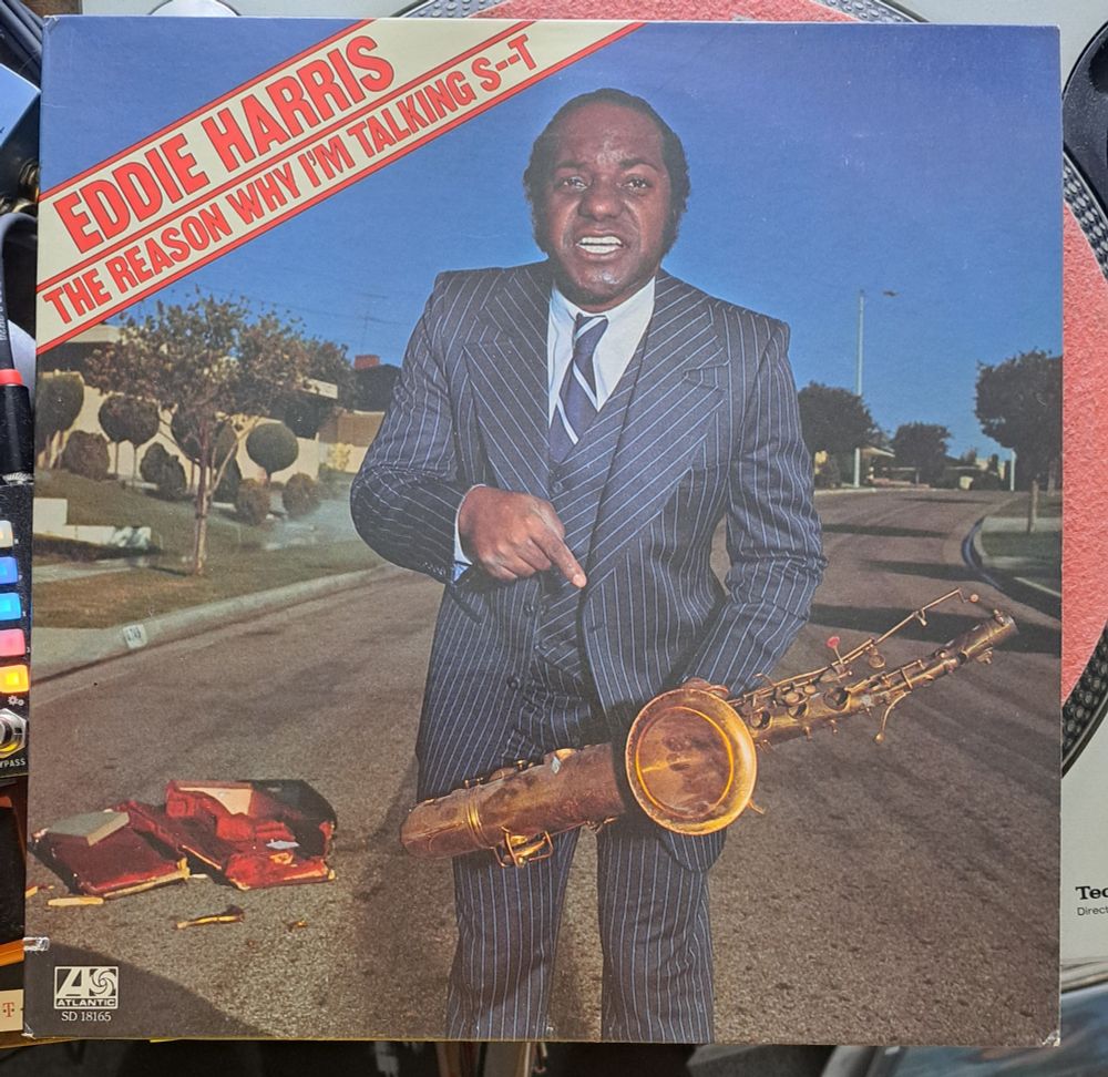 Record sleeve for Eddie Harris - the reasons why I'm talking shit. A balding middle aged black man in a blue suit stands in the middle of the road holding a saxophone and looking irritated.