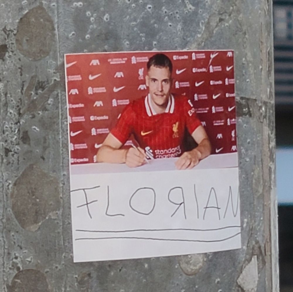 Der Sticker zeigt oben ein Bild von Florian Wirtz bei der Vertragsunterzeichnung in Liverpool, darunter eine kindlich gekrakelte und schief doppelt unterstrichende Unterschrift, die sich "FLORIAN" mit umgekehrten R liest.