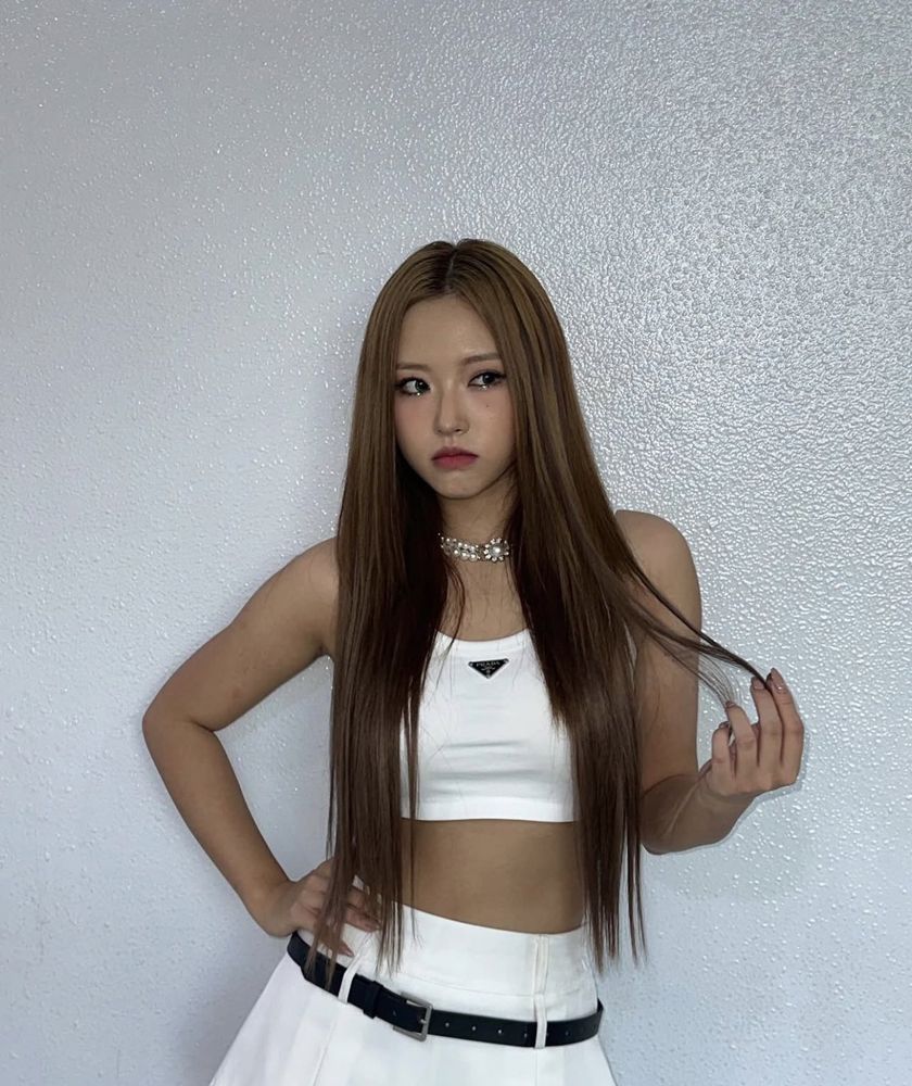 hyeju with her hair down in a white top and skirt with a black belt playing with her hair