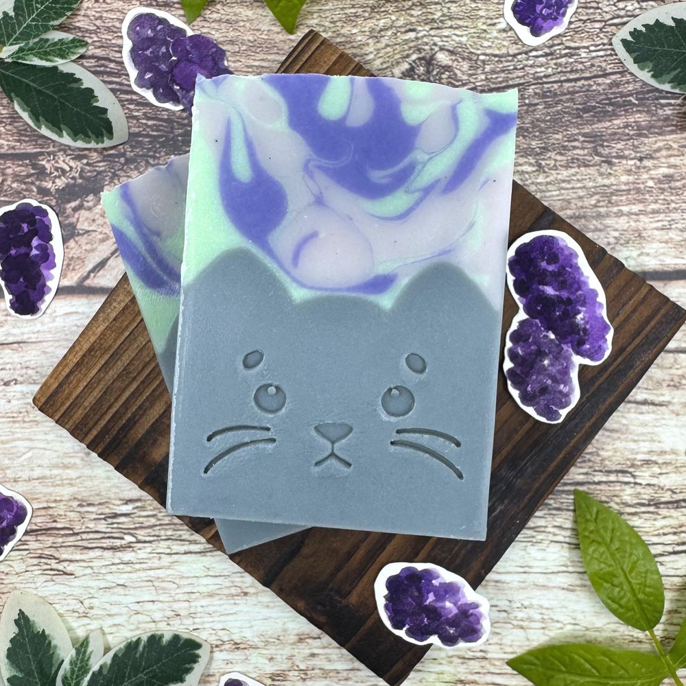 Two bars of handmade soap shaped in the form of gray cats with an uwu expression on its face.