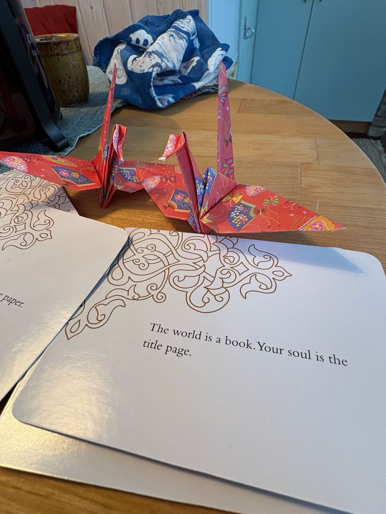 Index card with Rumi quote: the world is a page. Your soul is the title page

Red origami crane on brown table, coffee in the background.