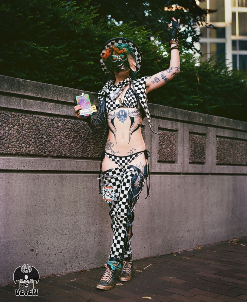 It's a film photo of Schmitty Britches at Anthrocon 2025. He is posing, showing off his wonderful outfit that has a checkerboard pattern. 