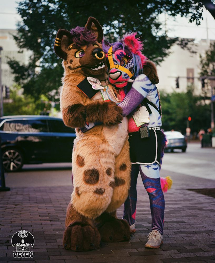 It's a film photo of two fursuiters at Anthrocon 2025. They are hugging. 